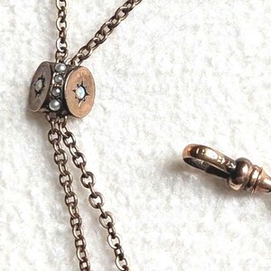 May include: Close-up of an antique bronze-toned necklace with a decorative central element. The central piece features small pearls and star-shaped accents. The necklace has a chain and a clasp.