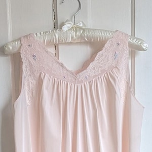 May include: A pale pink nightgown with a V-neck and lace trim. The sleeveless gown hangs on a satin-covered hanger against a white door. The nightgown has a flowing, lightweight design.