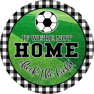 May include: A round sign with a soccer ball graphic and the text "IF WE'RE NOT HOME check the field." The sign has a green background with a soccer field image and a black and white checkered border.
