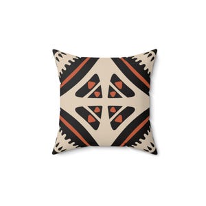May include: A square throw pillow with a geometric pattern in black, orange, and beige. The pattern features a repeating design of triangles and diamonds.