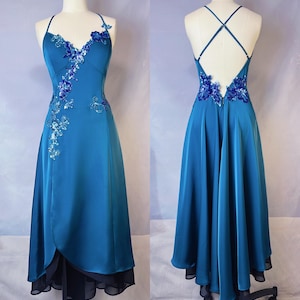 May include: Teal-colored formal dress with a flowing skirt and a halter neckline. The bodice and back feature floral embellishments. The dress has a layered skirt with a black underlay. The dress is displayed on a mannequin.