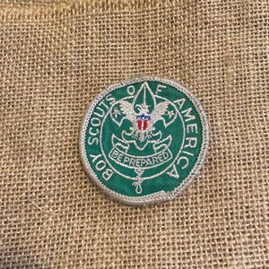 Peut inclure: Un écusson circulaire des Boy Scouts of America avec une bordure verte et des coutures blanches. L'écusson présente un emblème d'aigle blanc avec des accents rouges, blancs et bleus, et les mots "Boy Scouts of America" et "Be Prepared".