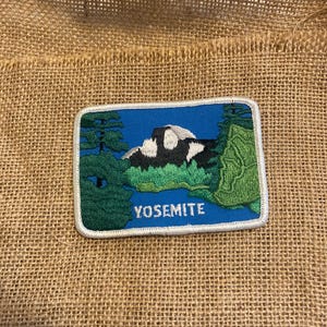 Peut inclure: Écusson brodé représentant le parc national de Yosemite. Le patch a un fond bleu avec une montagne, des arbres et le mot "YOSEMITE" en blanc. Le patch est bordé d'une couture blanche.