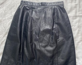 Può includere: Una gonna in pelle nera con una classica silhouette a trapezio. La gonna presenta una finitura liscia e opaca e un design semplice e pulito. La gonna è un capo versatile per ogni guardaroba.