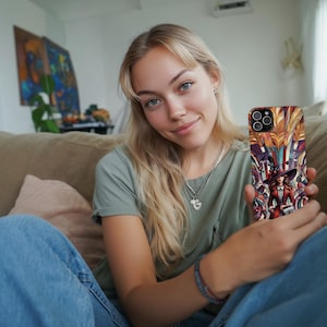 Può includere: Custodia per telefono colorata con una donna in cappotto e cappello rossi, su uno sfondo artistico vibrante. La custodia, tenuta da una persona, presenta un design nei toni del rosso, arancione, giallo e viola, con finitura lucida.