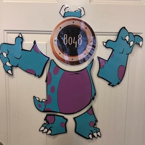 Puede incluir: Un recorte de monstruo azul y morado con una puerta redonda con el número 8048. El monstruo tiene tres brazos y tres piernas.