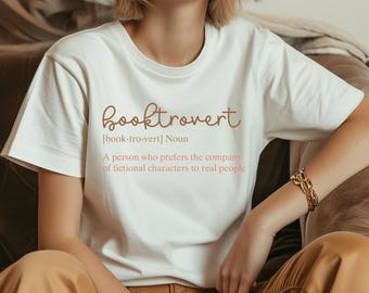 以下が含まれることがあります： 「booktrovert」というテキストと定義が書かれた白いTシャツ。「[book-tro-vert] 名詞 架空の人物との付き合いを、現実の人々よりも好む人。」