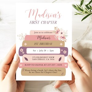 Puede incluir: Una tarjeta de invitación blanca con el texto "Madison's FIRST CHAPTER" en escritura rosa. El diseño presenta una pila de libros en tonos rosa, morado y beige, con detalles florales. La tarjeta anuncia una celebración de primer cumpleaños.