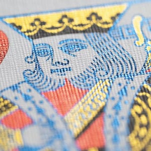 May include: A playing card with a red heart suit and a king of hearts illustration. The king is wearing a gold crown and blue and gold armor. The card has a textured surface.