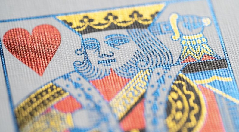 May include: A playing card with a red heart suit and a king of hearts illustration. The king is wearing a gold crown and blue and gold armor. The card has a textured surface.