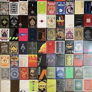Puede incluir: Una colección de 60 barajas de cartas diferentes, con una variedad de diseños y temas. Las barajas están dispuestas en una cuadrícula, con cada baraja mostrada en su embalaje original. Algunos de los diseños incluyen calaveras, animales y patrones geométricos.