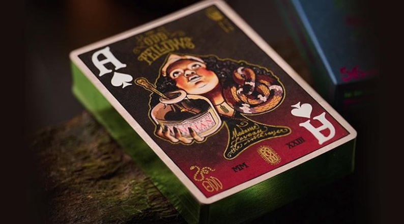 May include: A playing card from the Odd Fellows deck, featuring a woman with a snake wrapped around her arm, holding a jar labeled "Mysteries". The card is the Ace of Spades and has a red background with gold accents.