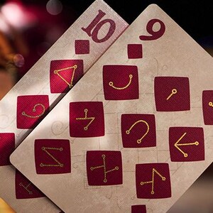 May include: Two playing cards, a nine and a ten, with a cream background and red squares containing gold symbols. The cards are from a deck with a unique design.