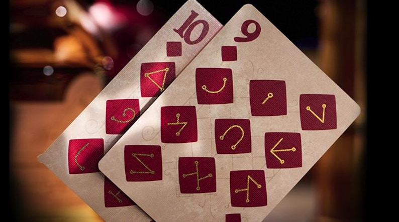 May include: Two playing cards, a nine and a ten, with a cream background and red squares containing gold symbols. The cards are from a deck with a unique design.