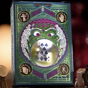 May include: A deck of playing cards with a green, purple, and silver design. The box features a spooky face with a crystal ball in the center. The text on the box reads "The Odd Fellows" and "Made in the USA".