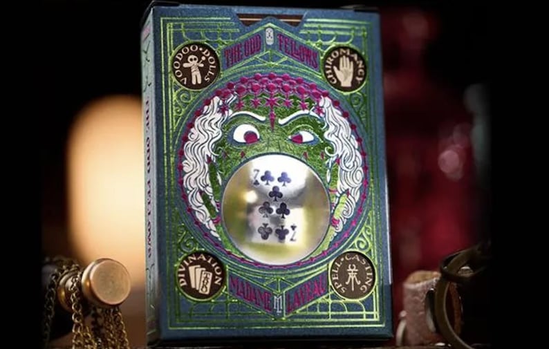 May include: A deck of playing cards with a green, purple, and silver design. The box features a spooky face with a crystal ball in the center. The text on the box reads "The Odd Fellows" and "Made in the USA".