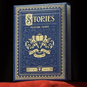 May include: A blue playing card box with gold lettering and accents. The box reads "STORIES PLAYING CARDS" and features an illustration of angels and an open book. The text "THERE ARE TWO SIDES TO EVERY STORY" is also visible.