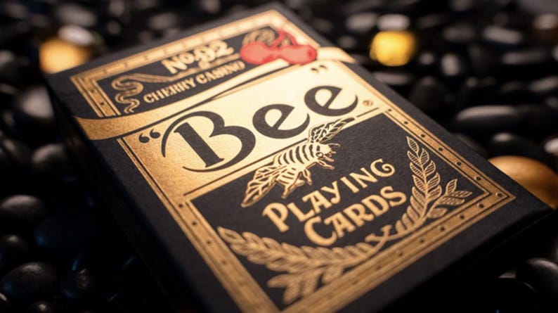 May include: A black box of Bee playing cards with gold foil accents. The box features the text "Bee Playing Cards" and a stylized bee illustration. The box also has a red cherry logo with the text "No. 92 Cherry Casino".