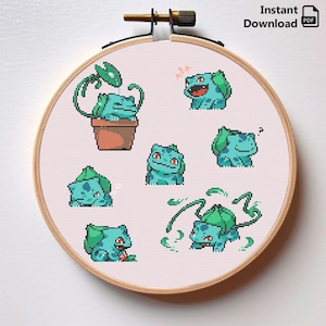 May include: A circular wooden embroidery hoop containing white fabric with a cross-stitch pattern featuring seven pixel-art style light blue and green creatures in various poses, including one sitting in a brown flower pot and others moving.