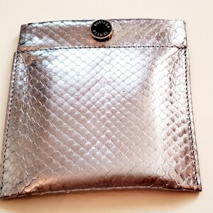Peut inclure: Pochette argentée avec un motif peau de serpent. La pochette est fermée par un bouton-pression avec l'inscription "BOTTEGA VENETA". Les bords sont cousus avec du fil noir.