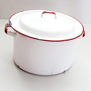 May include: White enamel pot with a lid, featuring red trim around the rim and handles. The pot has a rounded shape and a matching white lid with a red handle. A classic kitchenware item.