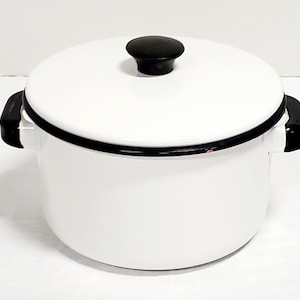 Può includere: Una pentola in smalto bianco con coperchio abbinato, caratterizzata da un bordo nero e manici neri su entrambi i lati. Il coperchio presenta un pomello centrale nero. La pentola ha una finitura liscia e lucida di forma cilindrica.