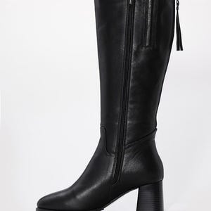 May include: Black knee-high boot with a block heel. The boot features a side zipper and a small tassel detail at the top. The leather boot has a pointed toe and a stacked heel.