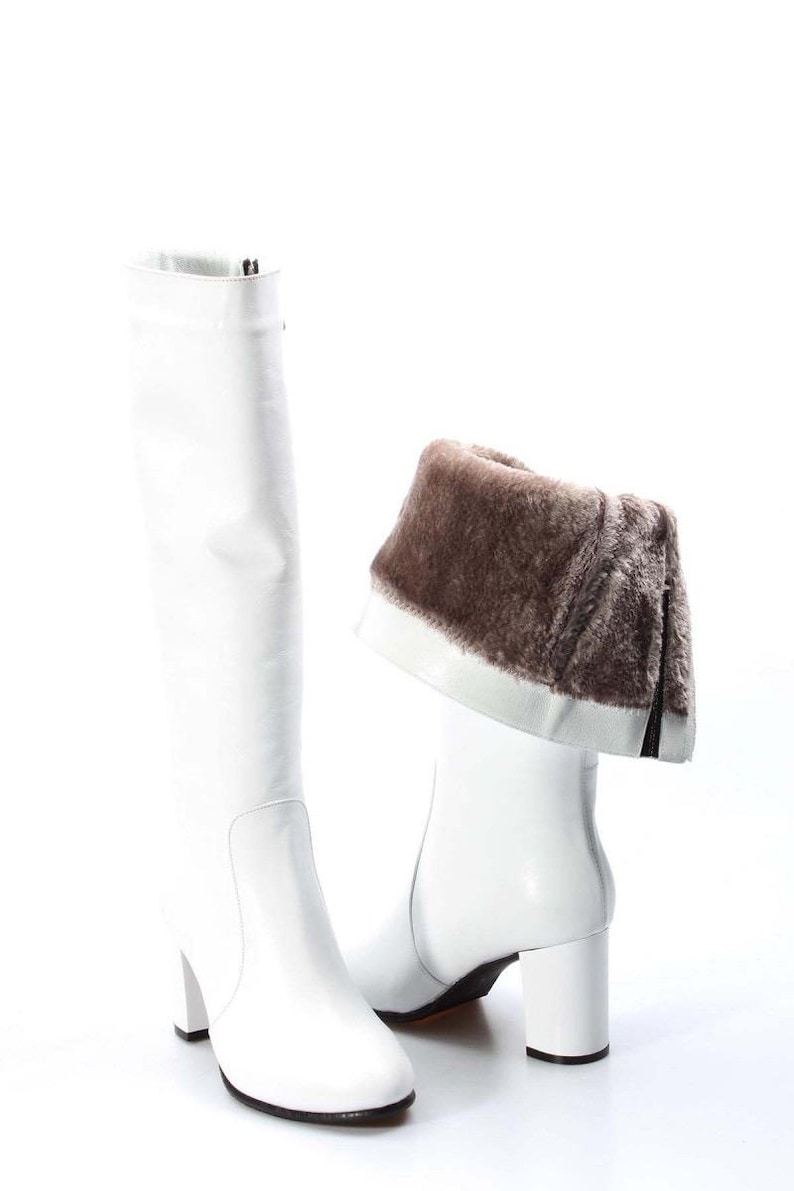 May include: White leather knee-high boots with a block heel and a brown faux fur trim around the top of the boot.
