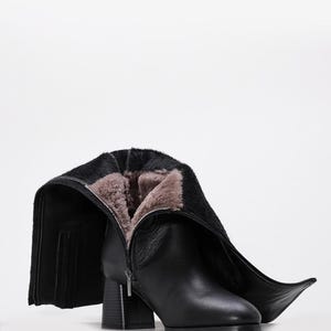 May include: Black leather boot with a block heel and a zipper closure. The boot's interior is lined with a light brown, furry material. The boot's shaft is folded down, revealing the interior lining.