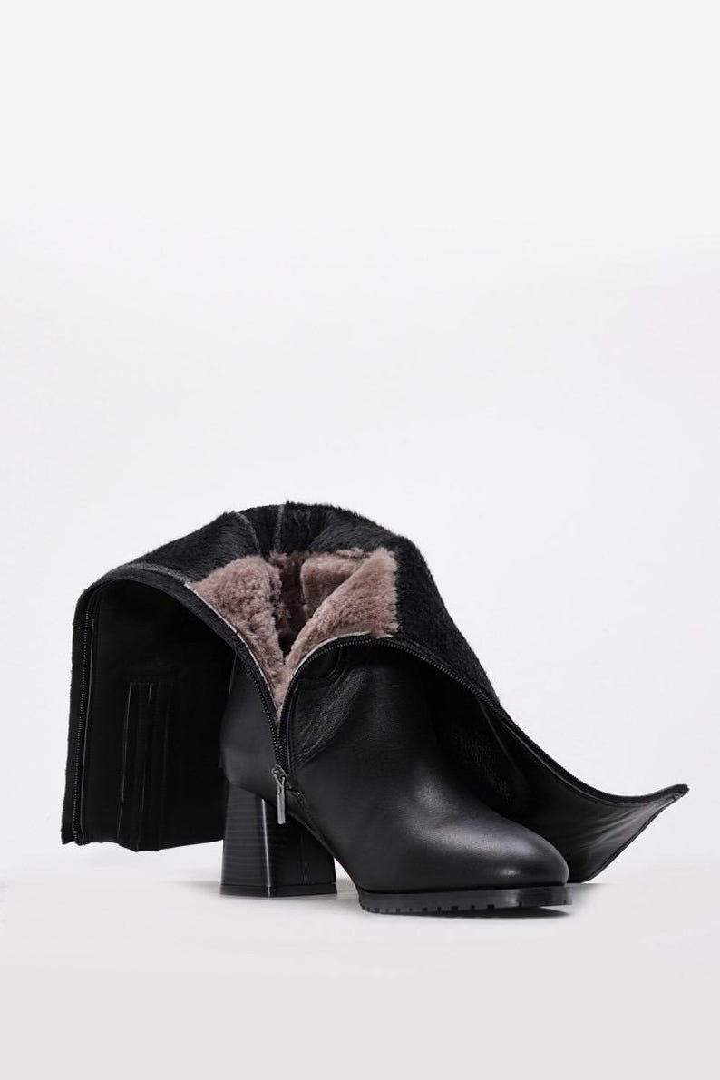 May include: Black leather boot with a block heel and a zipper closure. The boot's interior is lined with a light brown, furry material. The boot's shaft is folded down, revealing the interior lining.