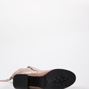 May include: A tan leather boot with a black sole and a block heel. The boot has a zipper on the side and a strap detail. The sole has a textured pattern. The heel measures approximately 3 inches.