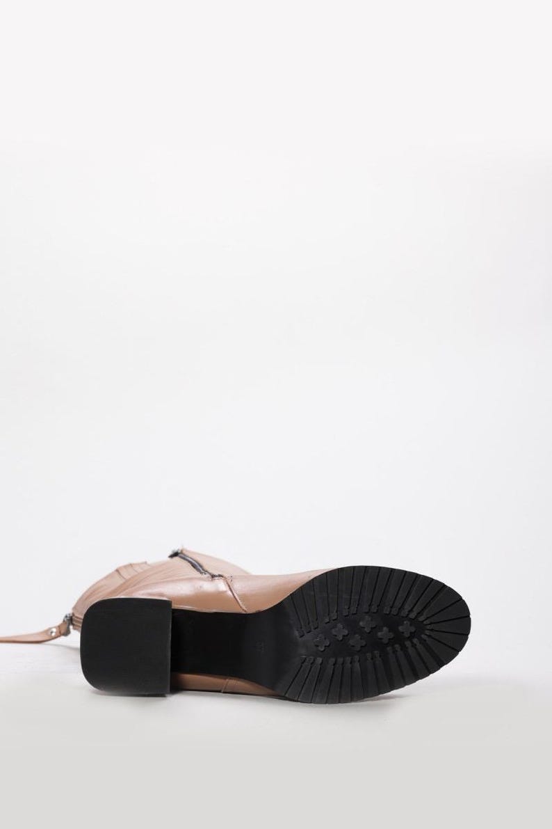 May include: A tan leather boot with a black sole and a block heel. The boot has a zipper on the side and a strap detail. The sole has a textured pattern. The heel measures approximately 3 inches.