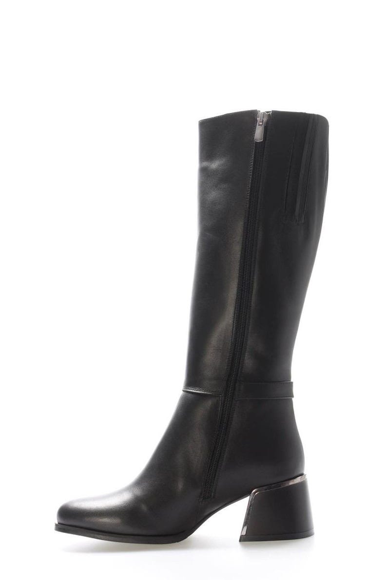 May include: Black leather knee-high boot with a square toe and a block heel. The boot features a side zip and a strap detail around the ankle. The heel is approximately 7.6 cm high.