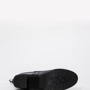 May include: Black leather boot with a block heel and a textured sole. The boot is lying on its side, showcasing the sole's tread pattern. The heel is approximately 3 inches high.
