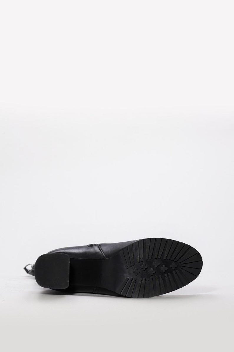 May include: Black leather boot with a block heel and a textured sole. The boot is lying on its side, showcasing the sole's tread pattern. The heel is approximately 3 inches high.