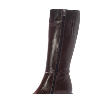 May include: A tall, brown leather boot with a side zip. The boot features a block heel and a textured finish. The zip runs along the side. The boot is approximately 35.5 cm tall.