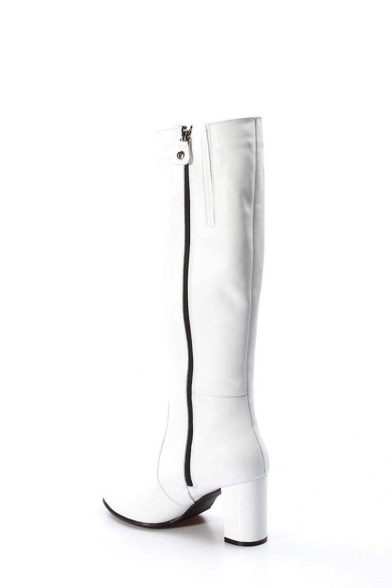 May include: White leather knee-high boots with a black zipper up the back and a block heel.
