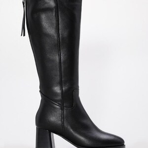May include: Black knee-high boots with a block heel. The boots have a zipper on the back with a small pull tab. The leather boots have a pointed toe and a smooth finish. The heel is approximately 3 inches high.