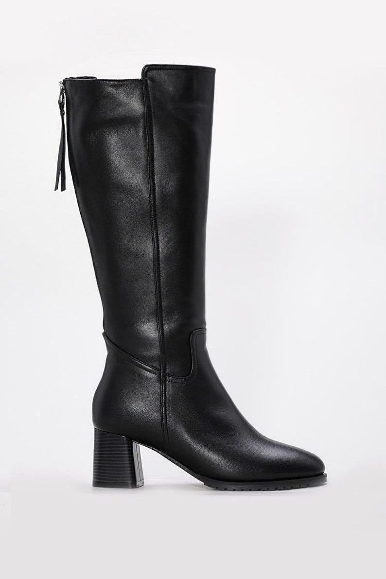 May include: Black knee-high boots with a block heel. The boots have a zipper on the back with a small pull tab. The leather boots have a pointed toe and a smooth finish. The heel is approximately 3 inches high.