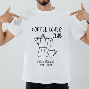 May include: White t-shirt with black text that reads "Coffee Lover Club" and a graphic of a coffee pot and a cup of coffee. The text below the graphic reads "Every Morning 7AM - 10AM".