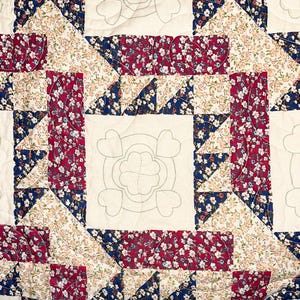 May include: A quilt with a patchwork design featuring a variety of floral fabrics in shades of red, white, and blue. The quilt is quilted with a simple stitch pattern and has a white background.