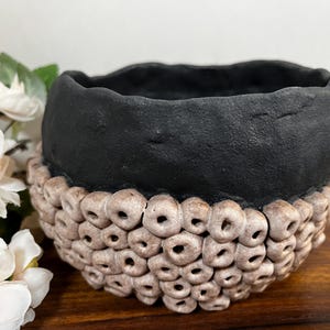 May include: A black ceramic planter with a textured rim and a unique design of small, raised circles around the bottom edge.