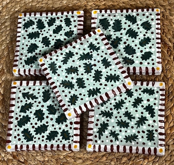 Hand-painted ceramic Christmas coasters with leaves and berries — genuine ceramics craft, whimsical holiday art, and at $85 for a set of 5 this is artisan pricing that signals real skill.