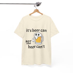 Può includere: Una maglietta beige con una grafica nera che dice "it's beer can not beer can't". La grafica include anche una lattina di birra di cartone animato con un viso.