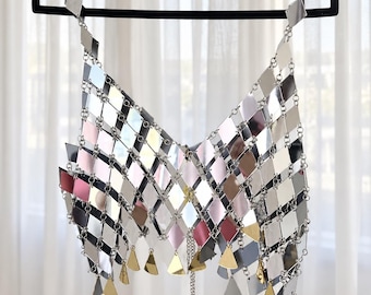 May include: A sleeveless top constructed from a grid of reflective, diamond-shaped silver, pink, and gold metallic plates connected by small metal rings. The garment features a V-neckline and a hemline accented with dangling triangular metal charms.