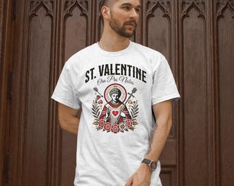 Puede incluir: Camiseta blanca con un gráfico de San Valentín sosteniendo un corazón. El gráfico es de estilo vintage con colores rojo, blanco y negro. El texto "St. Valentine Ora Pro Nobis" está impreso en la camiseta.