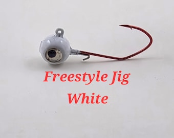 Może przedstawiać: Biała przynęta wędkarska Freestyle Jig z czerwonym haczykiem. Główka jigowa jest pomalowana na biało z dużym okiem. Tekst "Freestyle Jig White" jest czerwony.