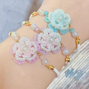 以下が含まれることがあります： パステルカラーのビーズフラワーブレスレット3本。ブレスレットは、白、ピンク、水色の花にパールとビーズのアクセントが付いています。ブレスレットは、ゴールドカラーの留め金が付いた白いコードに付いています。