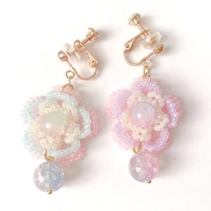 以下が含まれることがあります： パステルピンク、ブルー、ホワイトのビーズフラワーデザインのクリップオンイヤリングのペア。各イヤリングには、中央のビーズと、ぶら下がっている虹色のビーズが付いています。金属部品は金色です。