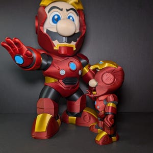 May include: Two red and gold action figures, one large and one small, resembling Mario in an Iron Man suit. The figures have blue eyes and a mustache. The larger figure is posed with an outstretched hand.